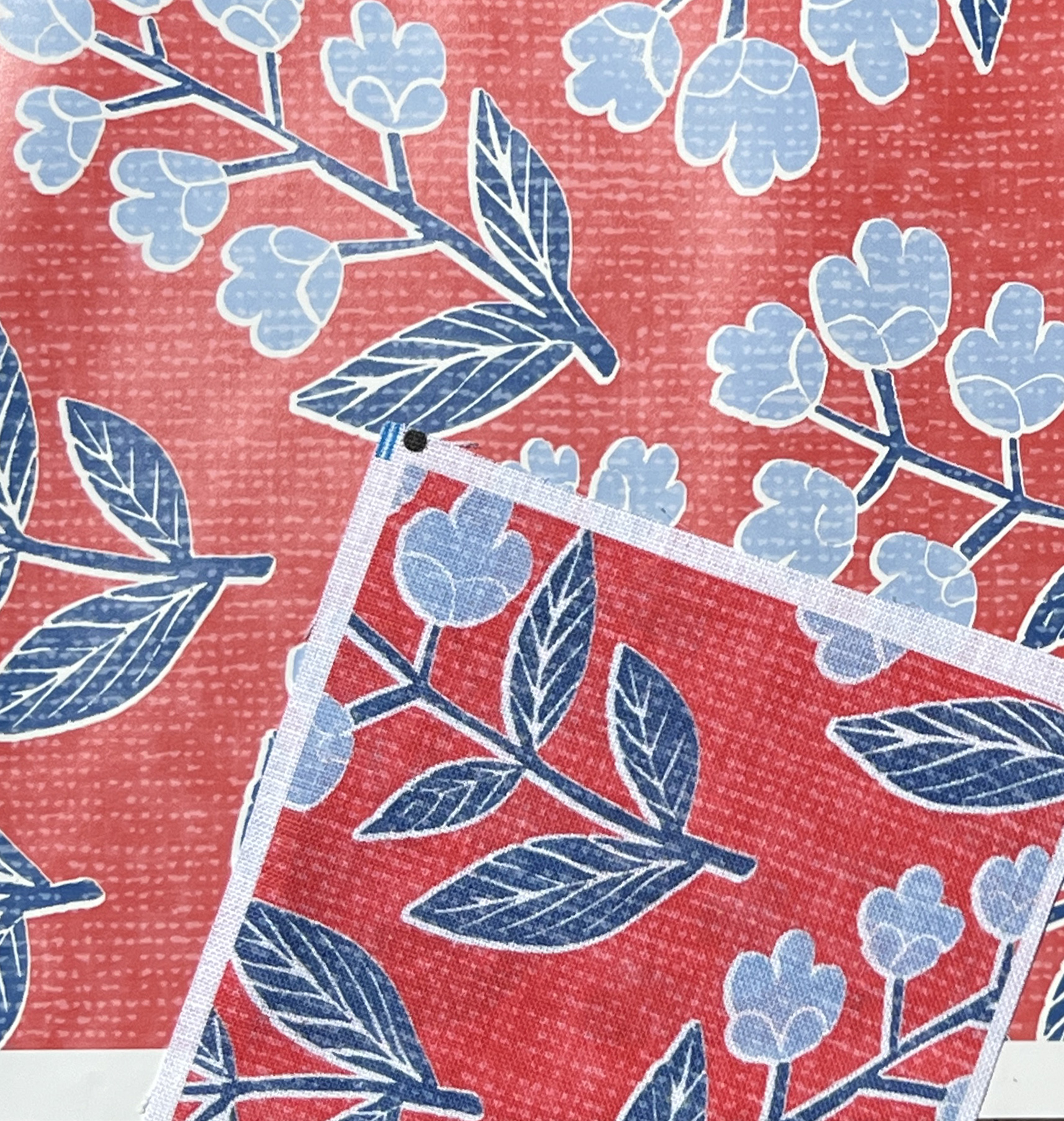 a blue floral design on a red background printed on shiny wallpaper compared to a matte swatch of the same design.