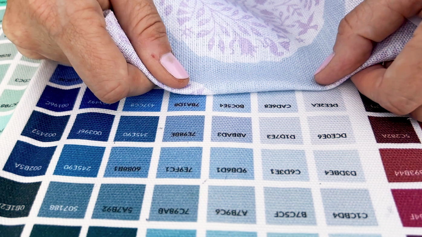 hands holding a paisley fabric design up to a color map with multiple squares of color with hex codes