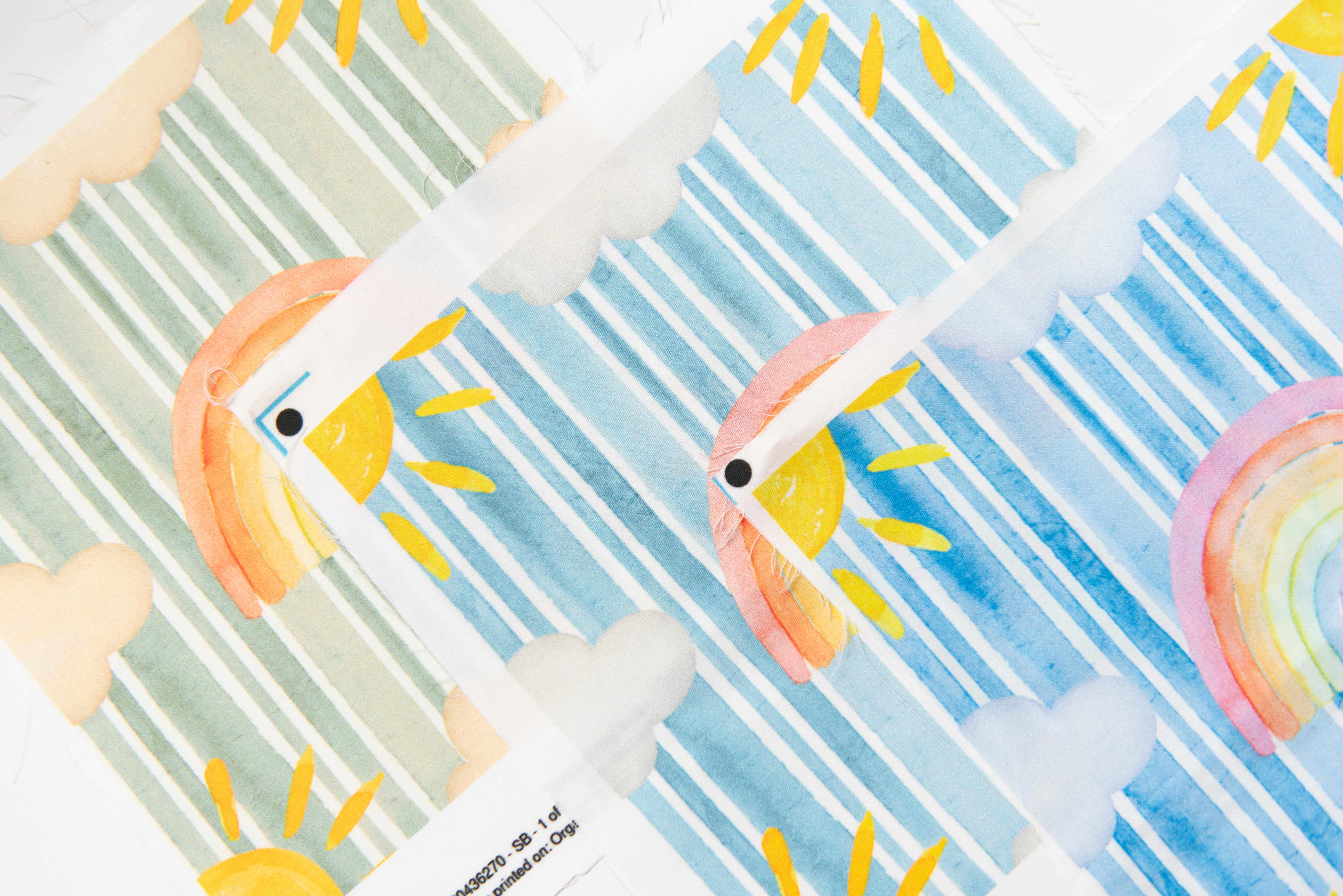 three swatches with a blue striped design with rainbows, clouds, and sun